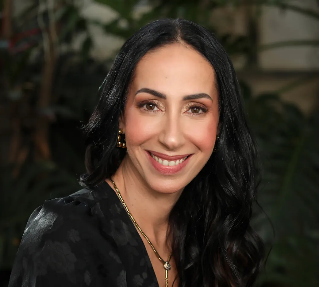 Retrato da Dra. Denise de Carvalho, sorrindo, com plantas ao fundo