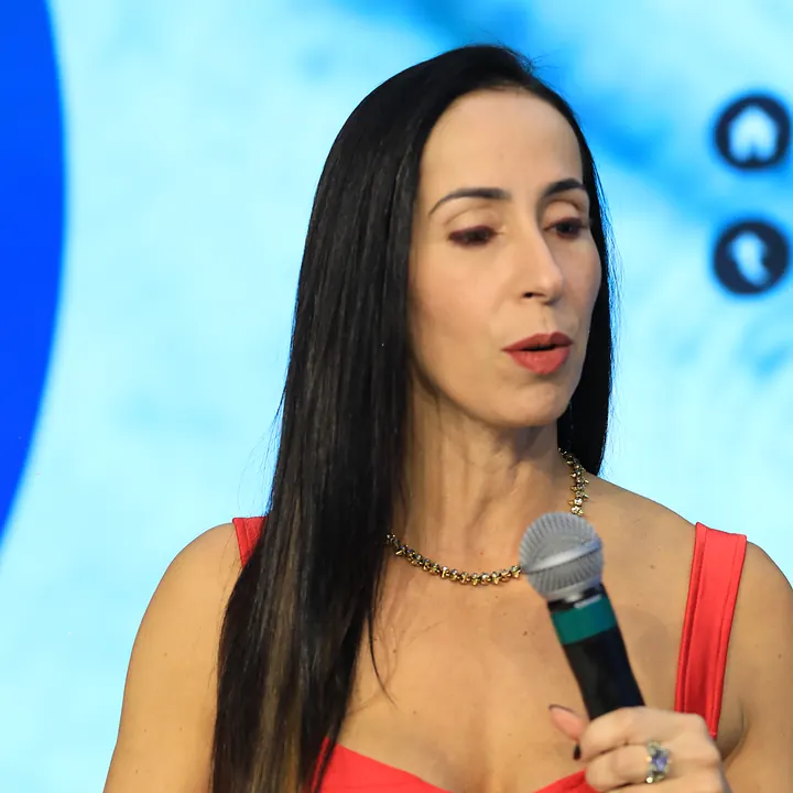 Dra. Denise de Carvalho com o microfone no palco, durante uma palestra